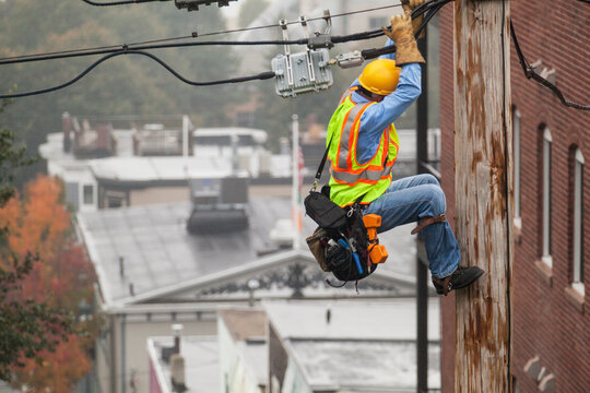 Cable lineman holding onto pole while using lineman spikes to adjust tension