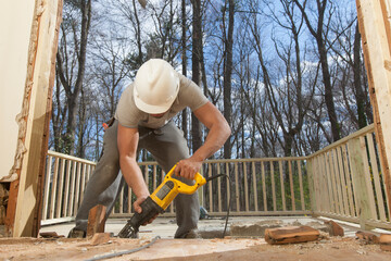 Hispanic carpenter using reciprocating saw to cut framing pieces for removal