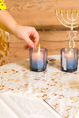 Fototapeta premium The hands of a Jewish woman light candles in honor of Shabbat on the table.