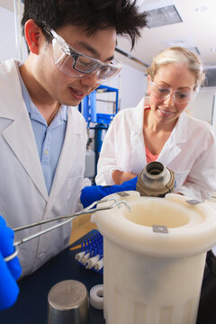 Engineering students using forceps while holding liquid nitrogen Dewar flask in water processing room in a laboratory