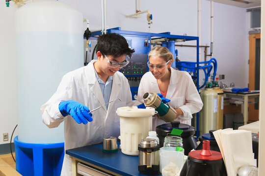 Engineering students using forceps while holding liquid nitrogen Dewar flask in water processing room in a laboratory
