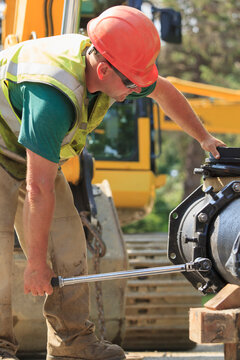 Construction worker using torque wrench to secure water main section with bolts