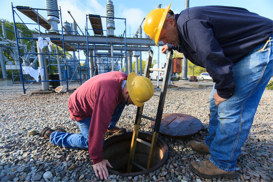 Power engineers placing ladder inside manhole at high voltage power distribution station