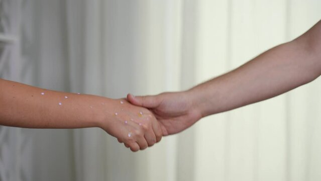 Unrecognizable ill woman and healthy man shaking hands in slow motion at white background. Young sick Caucasian lady with monkey pox rash handshaking with guy indoors