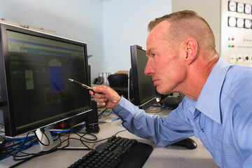 Engineer at electric power plant control room reviewing readings at management displays