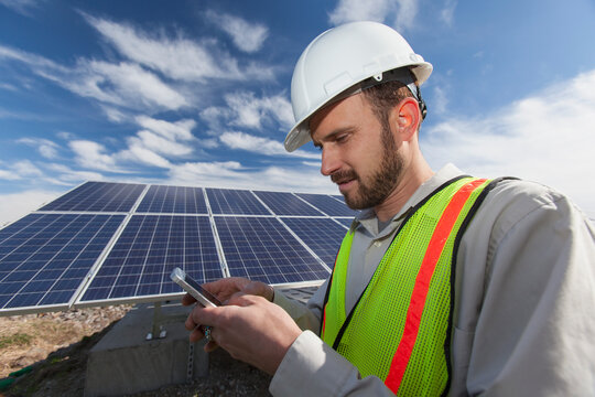 Power engineer texting on cell phone in front of solar photovoltaic array