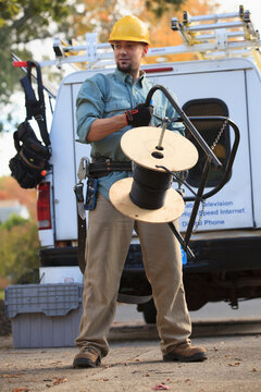 Tradesman holding cable for internet installation with work truck behind him
