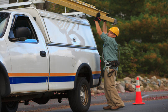 Lineman putting ladder back on truck at site