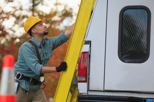 Lineman with ladder on truck at site