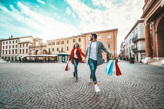 Happy beautiful young couple holding shopping bags walking on city street - Two loving tourists having fun on weekend vacation - Holidays and shopping concept