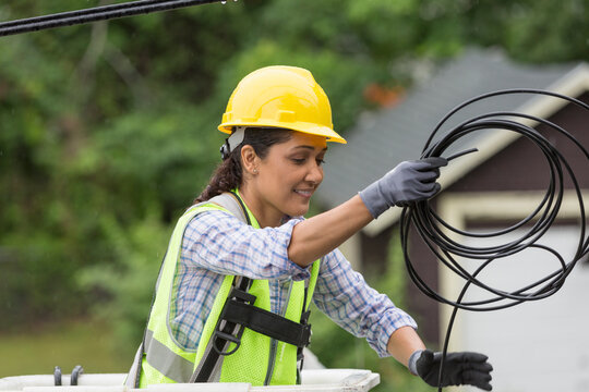 Hispanic female cable lineman stringing a new line in the rain