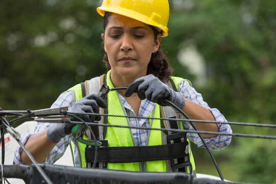 Hispanic female cable lineman crimping the cables in bucket lift