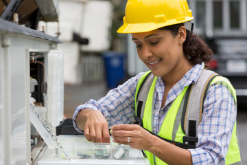 Hispanic female utility worker with box of cable amplifiers at site
