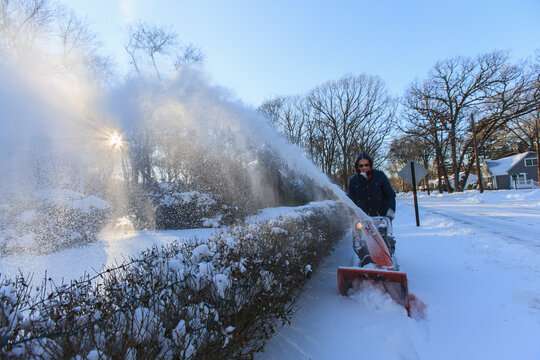 Middle aged man using snow blower after storm