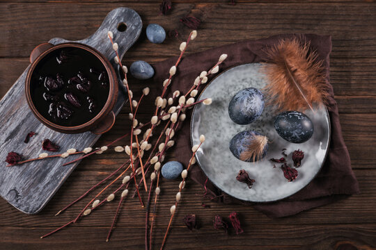 Dyed Easter eggs with marble stone effect painted with natural dye carcade tea from hibiscus flowers, pussy willow branches and feathers on dark wooden background.