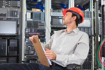 Network engineer with clip board reviewing control systems in data center