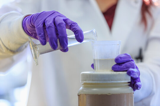 A scientist wearing purple gloves and pouring a solution into a container