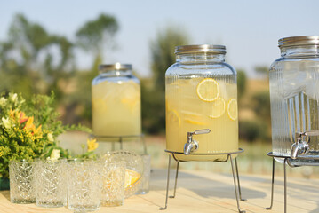 Natural lemonade dispenser with outdoor vintage glass cups - obrazy, fototapety, plakaty