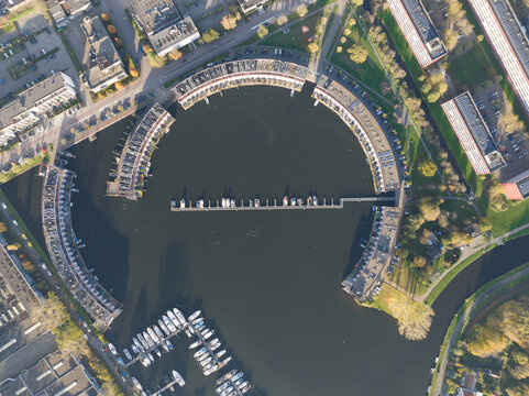 Harbour of Weesp, Aquamarin around the former industrial harbor. Suburban residential real estate housing in the shape of a circle. Small port recreactional living along the water. Aerial.