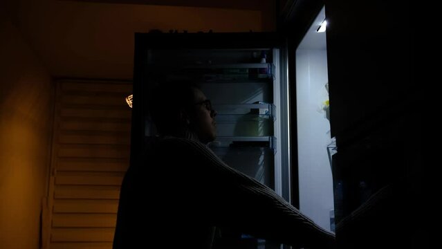 Young man looking for food in empty fridge or refrigerator at nighttime and showing his emotion sad, upset and angry.