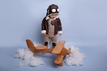 One year birthday party decorations. Little boy in helmet and glasses with wooden plane against the background of a blue wall. Happy child playing with toy wooden airplane. blue background
