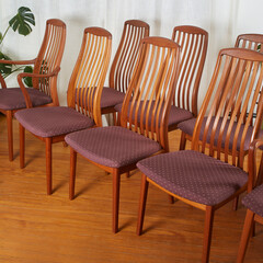 Dining chairs set, Mid-Century Modern design with purple seats, warm teak minimalist wood furniture. On display in a room with white curtains and large lively houseplants. 
