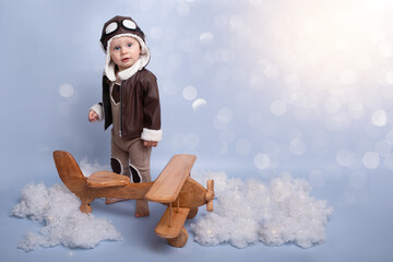 One year birthday party decorations. Little boy in helmet and glasses with wooden plane against the background of a blue wall. Happy child playing with toy wooden airplane. blue background