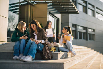 College friends are sitting on the stairs in front of the college building on a sunny day