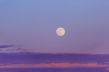 Full moon in a purple sky at dusk with a layer of clouds on the horizon; Surrey, British Columbia, Canada