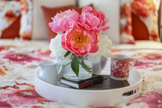 Bouquet of pink and white peonies on a bed tray with a coffee mug, journal and a creamer on top of a bed with floral patterned bedding; Surrey, British Columbia, Canada