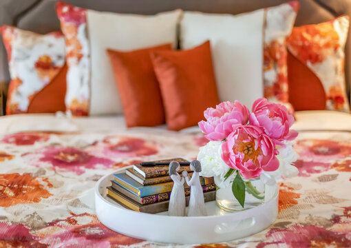 Bouquet of pink and white peonies, small stack of books and figurine on a bed tray  on top of a bed with floral patterned bedding; Surrey, British Columbia, Canada