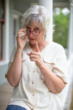 A mature woman looks over her eyeglasses wags her finger at the camera; Surrey, British Columbia, Canada