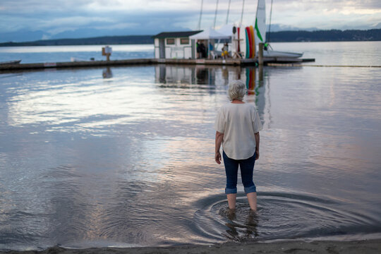 View taken from behind of a woman wading into the water from shore looking at gazebo at end of dock; Surrey, British Columbia, Canada