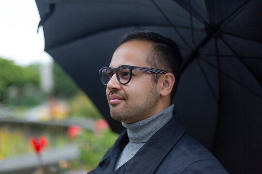 Close-up portrait of a man wearing eyeglasses standing under an umbrella looking outward; Surrey, British Columbia, Canda