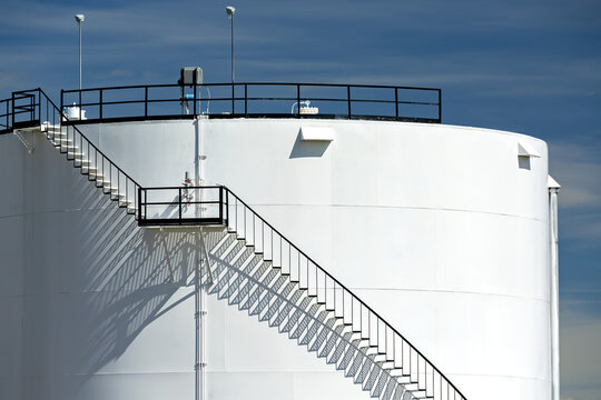 Close up of large white oil storage tank with black metal stairs with shadows and blue sky and clouds, North of Longview; Alberta, Canada