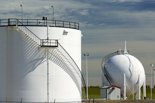 Close up of two large white oil storage tank with black metal stairs with shadows and blue sky and clouds, North of Longview; Alberta, Canada
