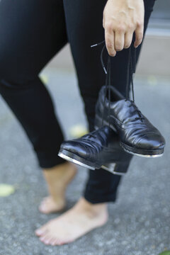 Close-up of dancer holding tap shoes and standing barefoot on ground outside; Langley, British Columbia, Canada