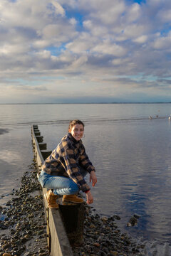 A young woman crouches on a narrow beam on Crescent Beach along the coast of BC; Surrey, British Columbia, Canada