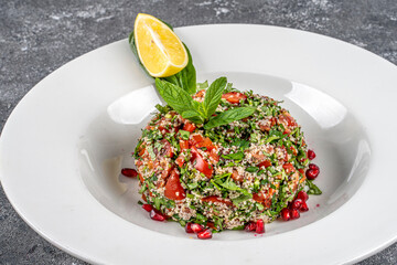 Traditional oriental salad Tabouleh with bulgur and parsley and tomatoe in a white plate on a wooden background.