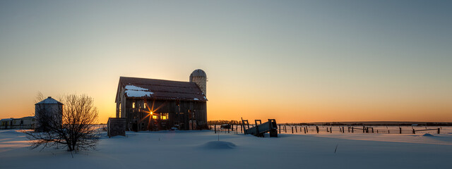 Dilapidated bard at sunrise in winter with a glowing yellow sky over the horizon seen through the abandoned barn; Rudyard, Michigan, United States of America