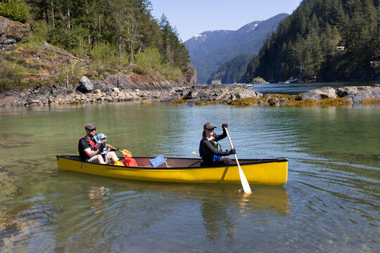 Young family going for a canoe ride along the coastline between Deep Cove Park and Twin Islands, along the West coast of Canada; North Vancouver, British Columbia, Canada