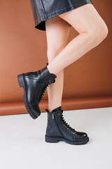 Female legs in a black skirt and high black leather boots. New collection of women's spring shoes