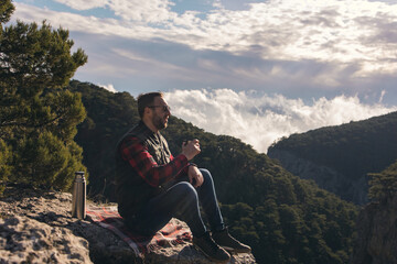 Man with beard taking rest in mountains after walk. Man is drinking hot drinks in mauntains. 