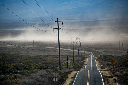 Utility poles line the Saddle Road, which crosses Hawai'i Island (Big Island) from Kona to Hilo and winds whipping up the dust; Hawaii Island, Hawaii, United States of America