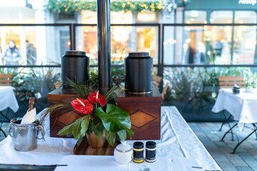 A table in a restaurant decorated with a red anthurium in a pot. A bottle of champagne in a bucket of ice and garland lights outside the window