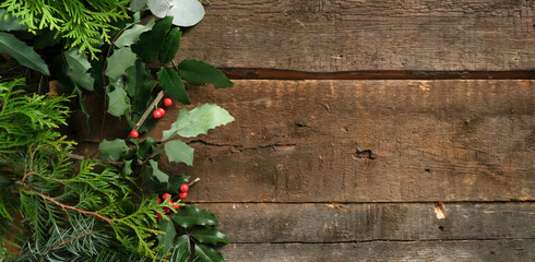 Christmas banner. Fresh spruce branches and holly on wooden background, copy space.