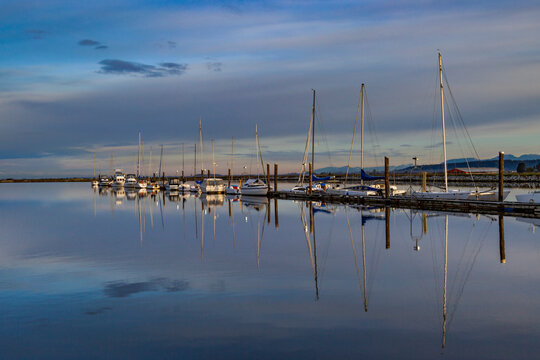 Mirror image of sailboat masts in tranquil water in a marina; Surrey, British Columbia, Canada