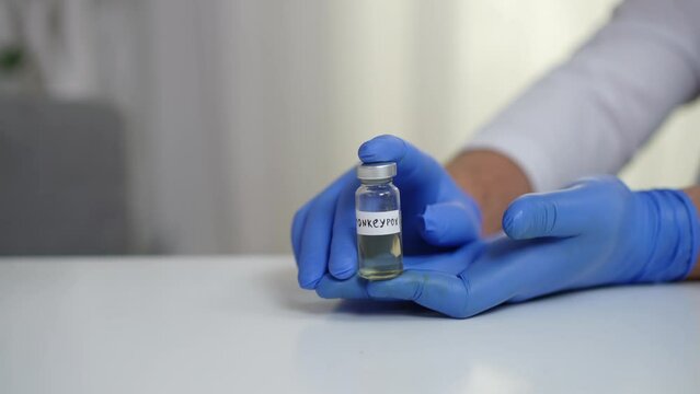 Unrecognizable doctor showing monkey pox vaccine in hospital. Caucasian professional scientist advertising transmissible contagious illness treatment sitting at table indoors