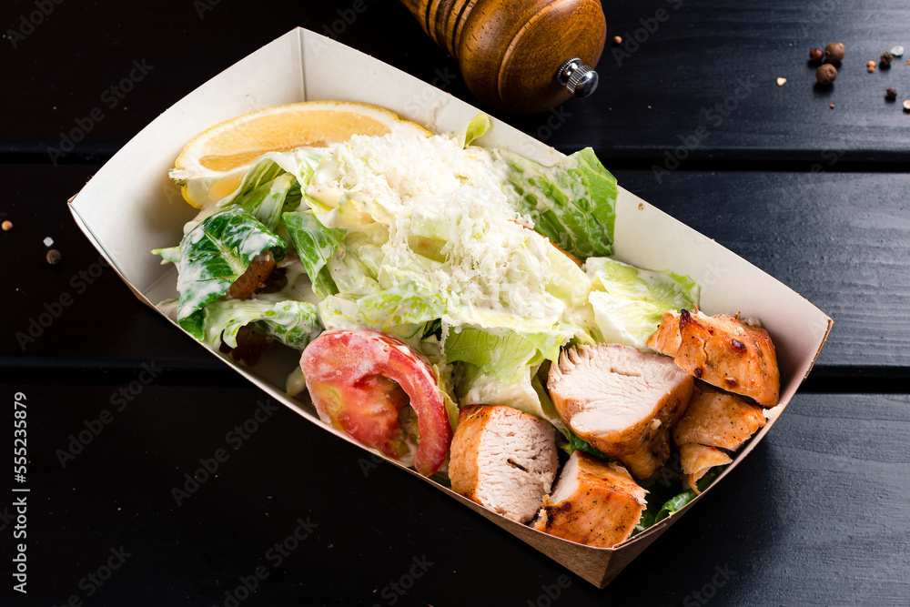 Sticker caesar salad with grilled chicken fillet in a takeaway box