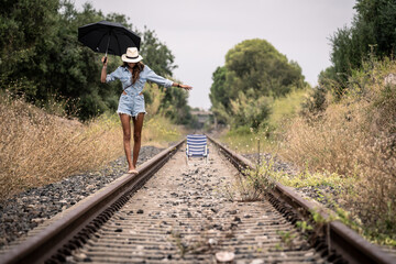 woman in cowboy dress with a black umbrella walking on a lonely railway